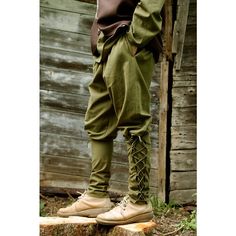 a man standing on top of a tree stump wearing green pants and brown shirt with laces