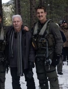 three men standing next to each other in the snow with trees and people behind them