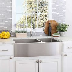 a kitchen with white cabinets and stainless steel sink in front of a window that looks out onto the trees outside