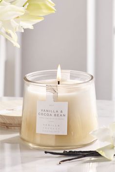 vanilla and cocoa bean candle sitting on top of a table next to a white flower