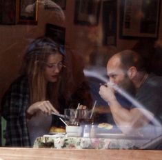 a man and woman sitting at a table in front of a window with food on it