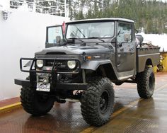 a large gray truck parked on top of a wet parking lot next to a white building