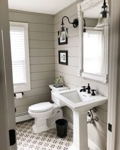 a white toilet sitting next to a sink in a bathroom under a mirror and light fixture