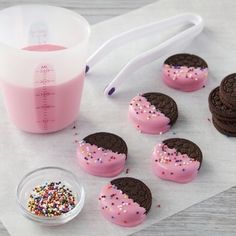 chocolate cookies with pink frosting and sprinkles next to a measuring cup