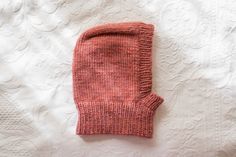 an orange knitted mitten laying on top of a white bed sheet with lace