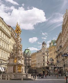 an ornate fountain in the middle of a city square with tall buildings and people walking around