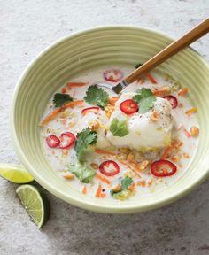 a green bowl filled with soup and garnished with cilantro, limes, red peppers, and sour cream