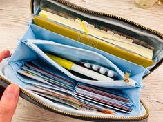 a person is holding an open wallet with pens and pencils in it on a table