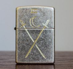 a lighter with two crossed spears on it sitting on top of a wooden table next to a wall