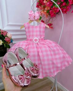 a hand holding a pink dress and matching pair of shoes with flowers in the background