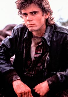 a man sitting on the ground with his hands in his pockets and wearing a leather jacket