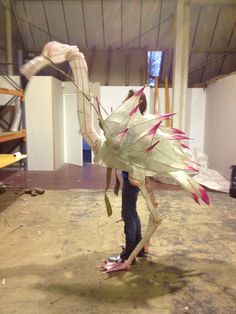 a woman standing in an unfinished room with a large bird costume on her head and arms