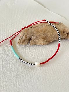 a white beaded bracelet sitting on top of a piece of wood next to a tree branch