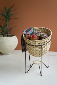 a wicker basket with several items in it sitting on a stand next to a potted plant