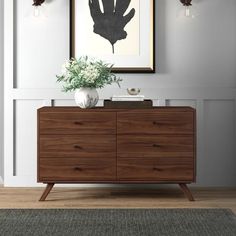 a vase with flowers on top of a wooden dresser next to a framed art piece