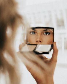 a woman is looking at her reflection in the mirror while holding a cell phone up to her face