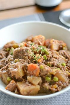 a white bowl filled with meat and vegetables on top of a table next to a cup