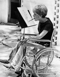 a young boy sitting in a wheel chair while holding an easel and drawing on a canvas