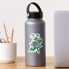 a metal water bottle next to a white laptop on a wooden table with pens and pencils