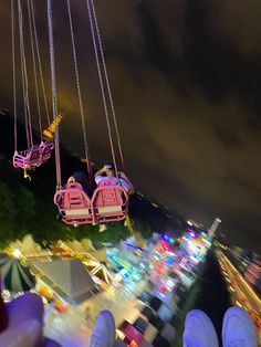 two pink chairs suspended over a carnival at night