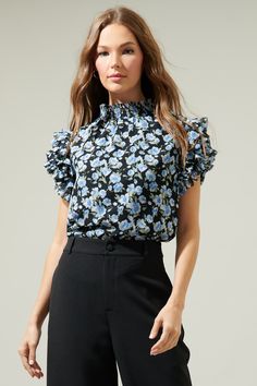 Standout like the prettiest flower of the bunch in the Endless Floral Mock Neck Ruffle Blouse! It features a smocked, mock neck. Ruffle layered short sleeves steal the show while framing a relaxed bodice that can be styled tucked into your favorite high waisted bottoms.- Mock neck- Ruffle layer sleeves- Lined- Keyhole- Color: Black BlueSize + Fit - Model is 5'8" and wearing size XS- Measurements taken from size S - Chest: 19 1/2"- Length: 24 1/2" Fabric Self:100% Polyester Lining:97% Polyester 3 Floral Print Stretch Tops For Work, Stretch Floral Print Tops For Work, Chic Top With Floral Print And Ruffled Collar, Black Ruffled Collar Top For Spring, Workwear Blouse With Floral Print And Flutter Sleeves, Flutter Sleeve Top With Floral Print For Work, Elegant Floral Print Stretch Blouse, Stretch Floral Print Blouse For Brunch, Fitted Blouse With Floral Print And Ruffle Sleeves