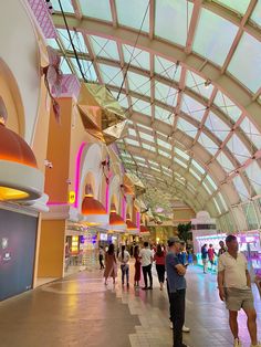 many people are walking around in an indoor shopping mall with colorful lights on the ceiling