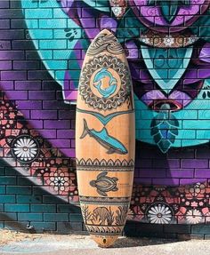 a wooden surfboard sitting in front of a brick wall with colorful graffiti on it