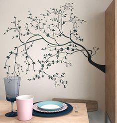 a dining room table with plates and cups on it, next to a tree wall decal