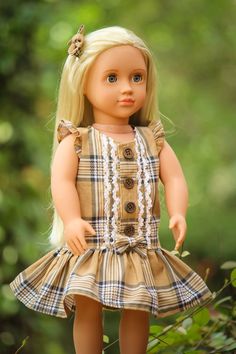 a doll with blonde hair wearing a brown plaid dress and white laces is standing in the grass