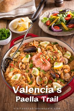 a red pan filled with rice covered in shrimp and clams next to other dishes