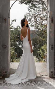 a woman in a white wedding dress is looking out an open doorway at the trees