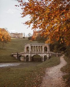 a stone bridge over a small stream in the middle of a field with trees around it