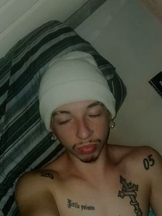 a shirtless man with his eyes closed wearing a white beanie and piercings