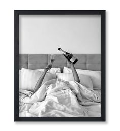 a black and white photo of a person laying in bed with a bottle of wine