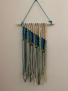 a wall hanging made out of yarn and wood with blue, white and green tassels