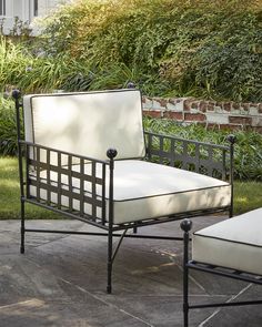 a chair and ottoman sitting on a patio next to a brick wall with bushes in the background