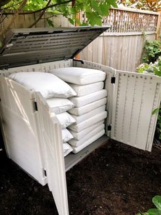 an open storage box filled with lots of white pillows in the dirt next to a wooden fence