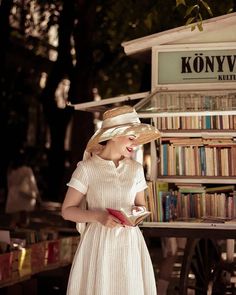 a woman in a white dress and straw hat standing next to a bookshelf