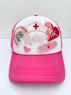 Pink and white Nurse themed trendy trucker hat. It says nurse with a rainbow, nurse hat, heart, bandaid & little heart. The pink is a cranberry type of medium pink color. This hat would be a great gift for a nurse!  This adult size hat was handmade by myself. The hat is made of fabric & foam with mesh along the back. It is easily adjustable in the back & has a ponytail holder. It is comfortable, lightweight & flexible. It fits the average adult size head, measuring about 8" diameter inside the hat.  Spot clean only. I don't recommend washing items with iron on patches because it'll weaken the adhesive glue under the patches.  Feel free to message me with any questions or if you would like to request a custom hat. Nurses Hat, Trucker Hat Ideas, Pink Trucker Hat, Nurse Hat, Band Aid, Small Business Ideas, Ponytail Holders, Custom Hats, Iron On Patches