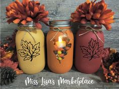 three mason jars decorated with fall leaves and candles