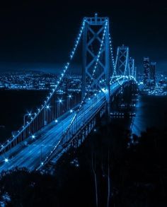 the bay bridge is lit up at night with blue lights on it's sides