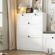 a white dresser sitting next to a window in a room with pictures on the wall