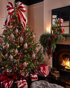 a decorated christmas tree with red and white striped bows in front of a fire place