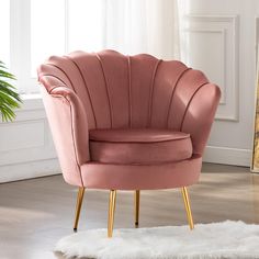 a pink chair sitting on top of a wooden floor next to a plant in a living room