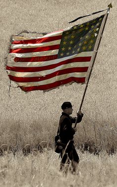 a man holding an american flag on top of a field