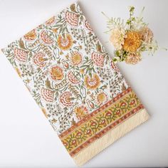 an orange, yellow and green floral print napkin next to a flower vase on a white surface