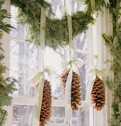 pine cones are hanging from the window sill in front of evergreen branches and ribbons