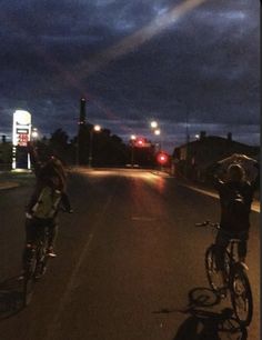 two people riding bikes down the street at night