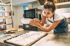 a woman in an industrial kitchen preparing food on top of a metal counter with a pan