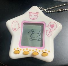 a white and pink star shaped digital clock on a silver ball chain hanging from a black table